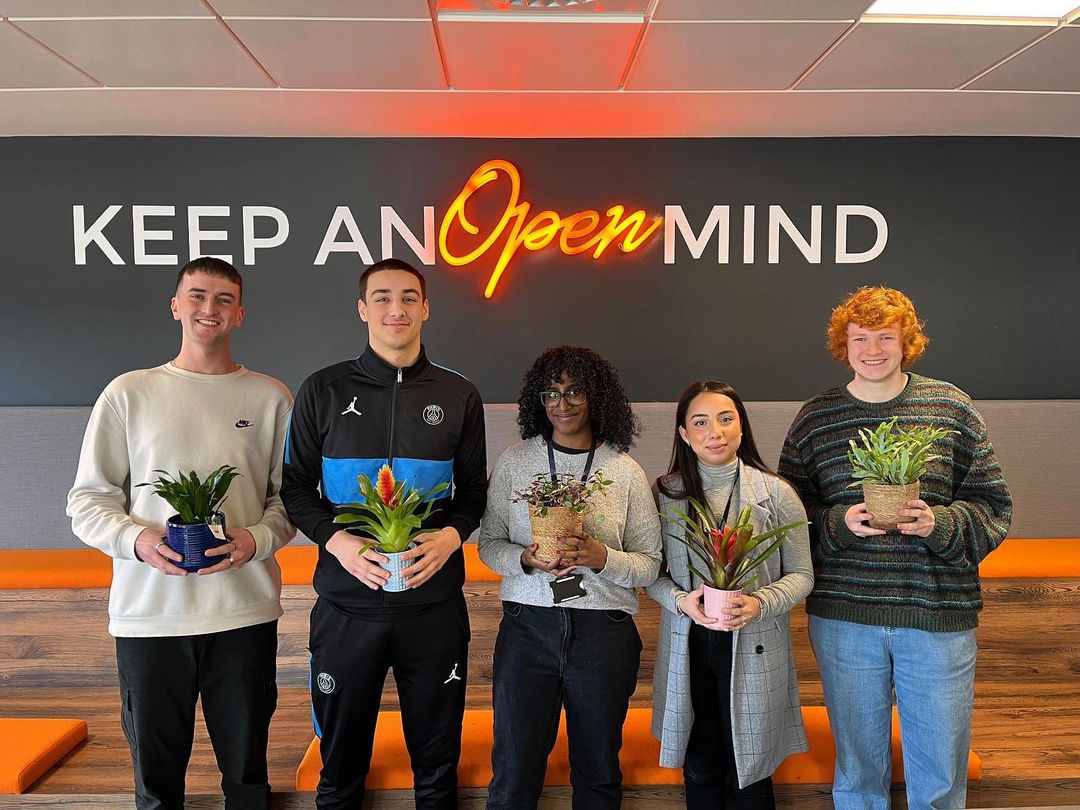 Apadmi employees holding pot plants under the office slogan “Keep an open mind”